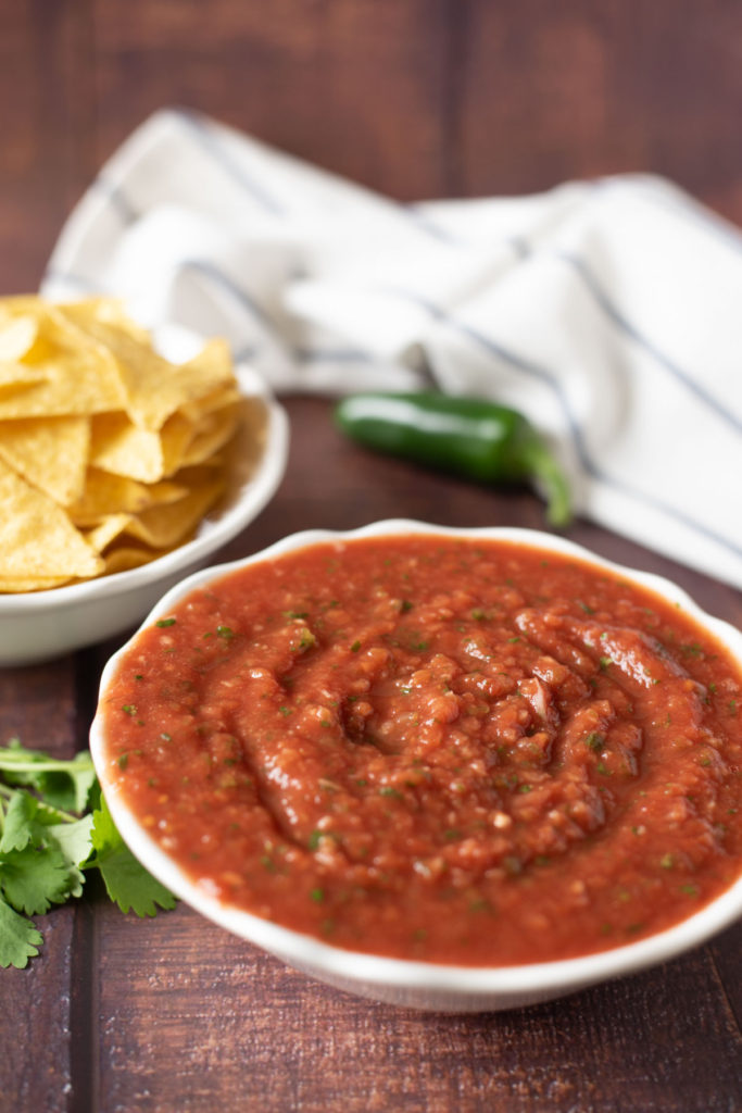 close up of salsa in a bowl with tortilla chips in the background